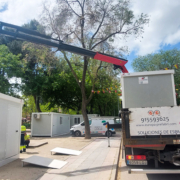 Vista frontal de dos módulos prefabricados tipo camerino instalados por Europa Prefabri para el Ayuntamiento de Pinto, con acceso independiente y acabados en blanco. En el entorno se aprecia una zona urbana destinada a actividades culturales.
