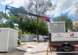 Vista frontal de dos módulos prefabricados tipo camerino instalados por Europa Prefabri para el Ayuntamiento de Pinto, con acceso independiente y acabados en blanco. En el entorno se aprecia una zona urbana destinada a actividades culturales.